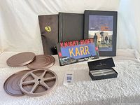 Group shot of all items: script, additional black volume, cinema book, film cans & reel, KARR plate, pen set