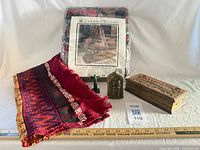 Group shot of afghan in package, red textile, green totem, metal icon, carved box with ruler for scale