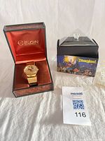 Elgin watch in open presentation box beside Disneyland bulb display case and outer box