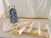 Front view of complete lot showing teapot on stand, five towels and ruler for scale