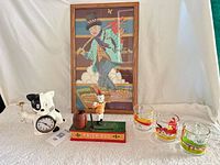 Group shot of all items: framed needlepoint, Trick Dog bank, cat clock, three Garfield glasses