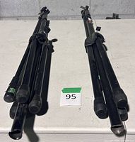 Two folded black metal tripod microphone stands with boom arms