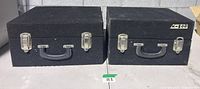 Front view of both black carpeted road cases with handles and latches visible