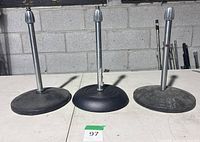 Three short nickel microphone stands with weighted round bases on tabletop