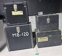 Four black wooden road cases of different sizes stacked two by two with visible latches, handles, labels
