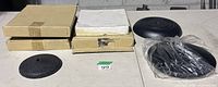 Seven black weighted round microphone stand bases, four in boxes, one unboxed, two in plastic