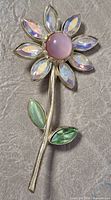 Front view showing pink cabochon, iridescent petals, green leaves