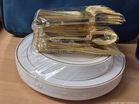 Stack of white plates with gold rim and bundled gold cutlery on top
