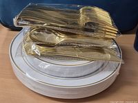 Stack of sealed plates with gold rim and bundle of sealed gold cutlery on top