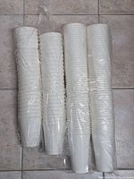 Four sealed sleeves of plain white disposable cups on tiled floor