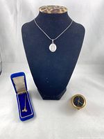 All three items: locket necklace on bust, stick pin in case, small clock insert