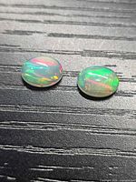 Two oval cabochon opals on dark textured surface showing play-of-color