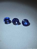 Three round faceted violet-blue stones on light background
