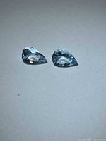 Two pear-cut light blue aquamarines on neutral background