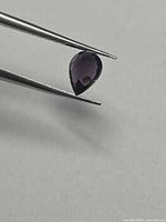 Pear-cut spinel held by tweezers showing front facet pattern and color