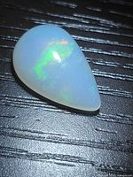 Pear-shaped opal on dark surface showing play-of-color.