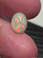 Front view of the oval Ethiopian opal on fingertip showing red, orange and green flashes