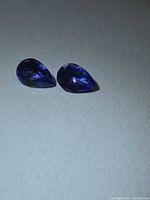 Two pear-cut deep blue tanzanites on neutral background