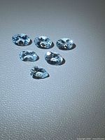 Six oval aquamarine gemstones on textured surface, showing size and colour
