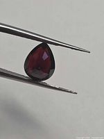 Pear-cut garnet held in tweezers side profile