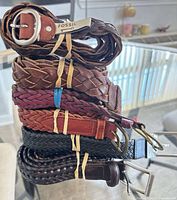 Stack of eight braided and woven leather belts showing colours and buckles