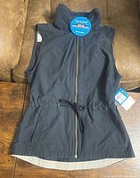 Front view of black Columbia vest laid flat showing zipper, drawstring waist, pockets, hang tags