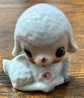 Front view of seated porcelain lamb figurine showing hand-painted face and pink flower