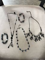 Group shot of all five jewelry pieces laid out: three necklaces and two bracelets