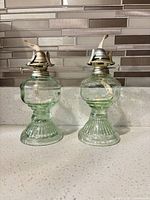 Front view of both light green glass oil lamps showing overall design and condition