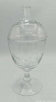 Full view of clear engraved glass apothecary jar with lid on plain backdrop
