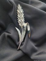 front view of silvertone wheat stalk brooch on dark fabric backdrop