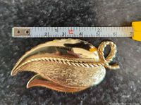 Front view of goldtone leaf brooch with tape measure showing approx 2.25 in. length