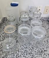 Group view of ten glass jars of varying shapes and one plastic beverage container