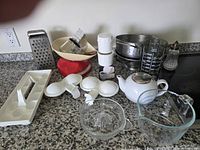 Group shot showing all kitchen gadgets including scale, teapot, measuring cup, juicer, egg poacher, grater, colanders, shaker and chopper