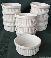 Stacked view of all 12 white ceramic ramekins showing fluted sides