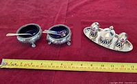 Group view showing two salt cellars, spoons and three-piece condiment set on tray with measuring tape for scale