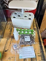 White AeroGarden unit with LED panel, accessories laid out including seed cups, labels, sponges, measuring cup