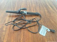 Full view of curling iron with cord on wooden surface
