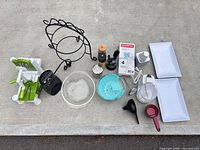 Overhead view of entire lot: mandoline, can opener, glass bowl, silicone steamer, boxed measuring cups, grinders, ladle, scoop, display stand, ceramic trays
