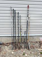 Full group of 13 adult hockey sticks leaning against siding