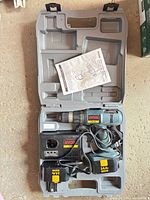 Open kit showing drill, charger, batteries, manual in carry case