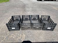 Four black plastic crates lined side by side on pavement