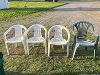 Front view of four plastic resin stackable armchairs, three white and one green, arranged outdoors