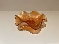 Oblique view of amber marigold carnival glass bowl showing ruffled rim and ball feet