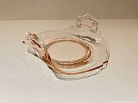 Oblique view of pink and clear glass candy dish showing handles, scalloped rim, footed base