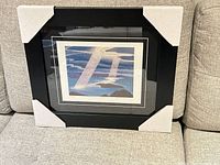 Framed lithograph with corner protectors on sofa