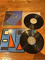 Both album jackets, both vinyl records and sleeves on wood surface