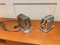 Two chrome electric toasters with cords on wooden surface