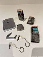 Group shot of cigarette case, three match holders, table lighter and three pocket knives