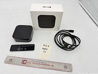 Apple TV 4K unit, Siri Remote, power cord and box with ruler for scale